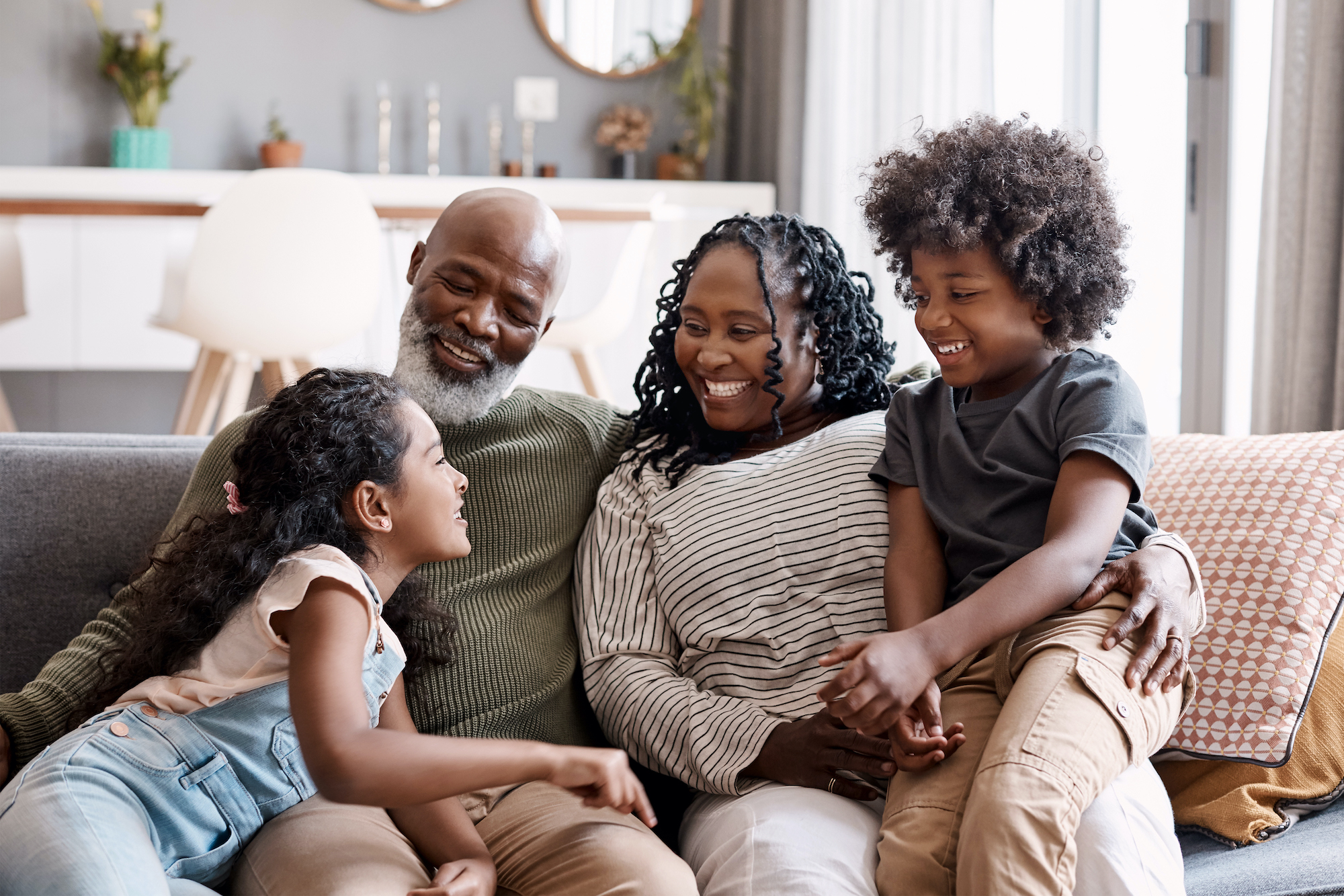 Two young siblings sit happily with grandparents on couch